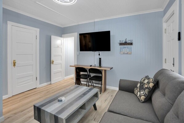 A living room with a gray sofa, a coffee table, a TV on a wooden stand, and two black chairs.