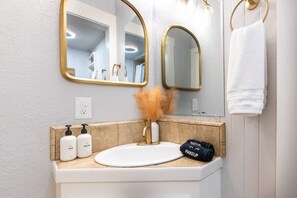 Une salle de bain avec un lavabo blanc, des robinets dorés et deux miroirs dotés de cadres dorés.
