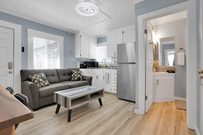 Ein modernes Wohnzimmer mit grauem Sofa, einem Couchtisch und einer Küchenzeile mit weißen Schränken und Geräten.