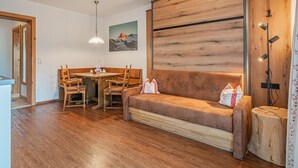 Una habitación acogedora con suelo de madera, un sofá, una mesa de comedor con sillas, una lámpara colgante y una pared de madera decorativa.