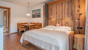 Un dormitorio con cabecera de madera, cama con ropa blanca, una mesa de comedor con sillas y una lámpara colgante.