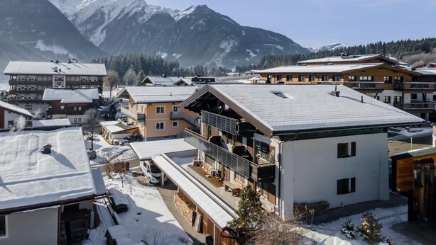 Un complejo turístico de montaña con varios edificios, incluyendo un hotel grande con balcones y un telesilla visible al fondo.
