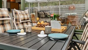 Un coin repas avec une table dressée pour deux personnes, agrémenté de coussins à carreaux, d’un panier de pain et d’un drapeau décoratif.