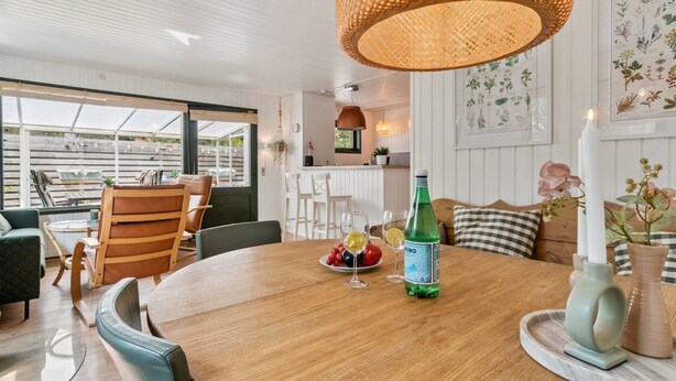 Un coin repas avec une table en bois, des chaises, une bouteille de gin, des verres et une bougie.