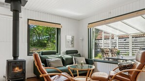 Une pièce chaleureuse avec un poêle à bois, un canapé vert, des fauteuils en cuir et une table en verre.