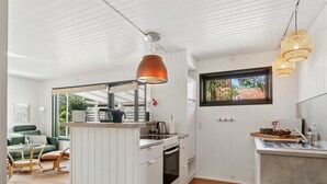 Une cuisine moderne avec des meubles blancs, un coin repas en bois et une fenêtre donnant sur un espace verdoyant.