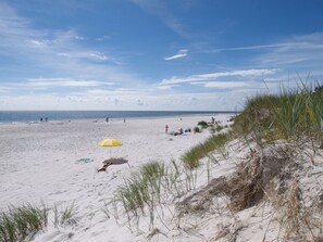 A sandy beach with a yellow umbrella, people, and dunes.