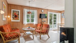 Un salon chaleureux avec des murs en bois, une cheminée, des meubles en osier et un téléviseur.