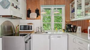 Une cuisine moderne avec des meubles blancs, un four à micro-ondes, un lave-vaisselle et une fenêtre donnant sur un espace verdoyant.