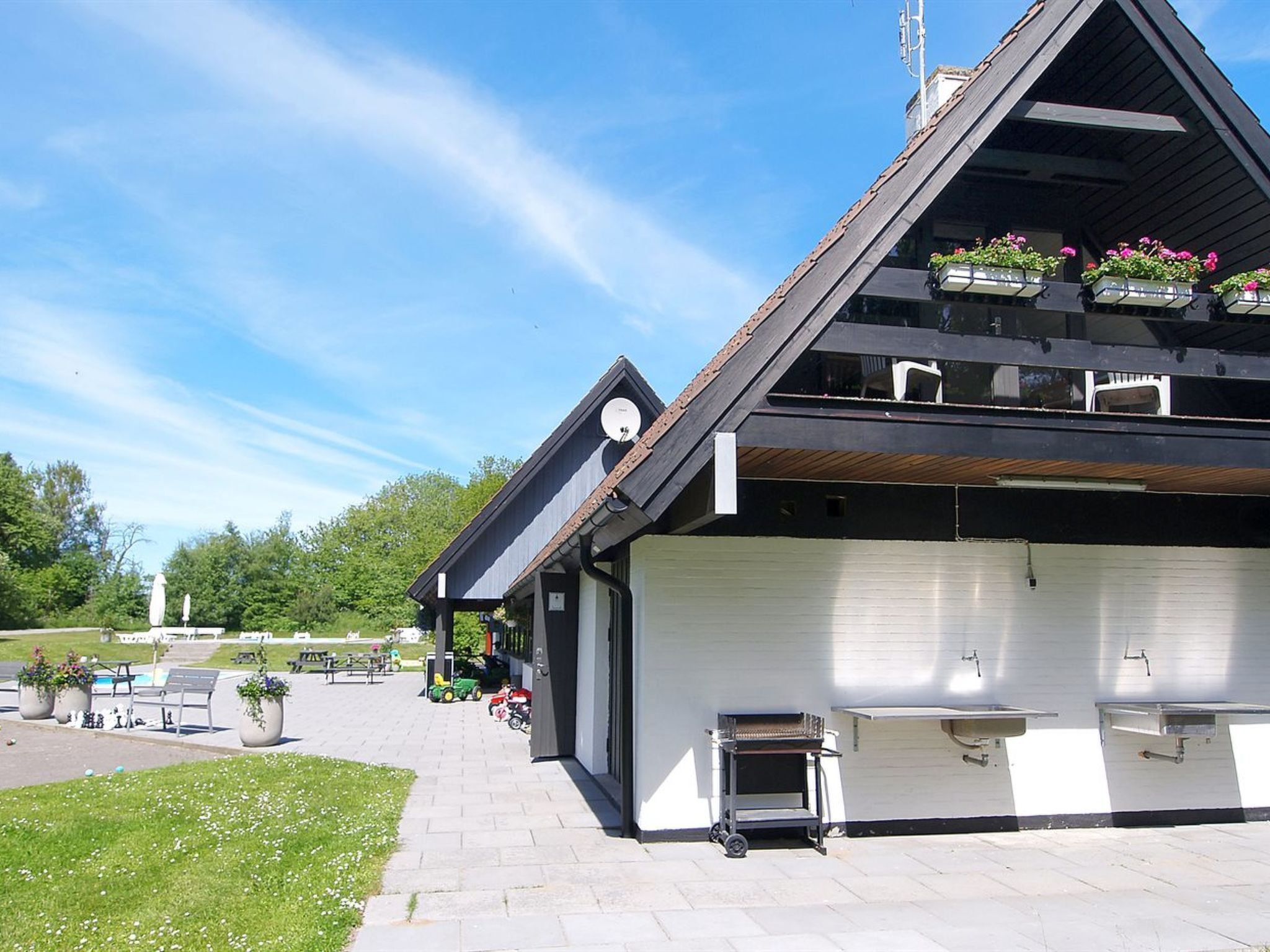 En moderne bygning med skråt tag, udendørs siddeplads og en overdækket terrasse.