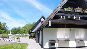 Un bâtiment moderne doté d’un toit en pente, d’un espace extérieur aménagé pour s’asseoir et d’une terrasse couverte.