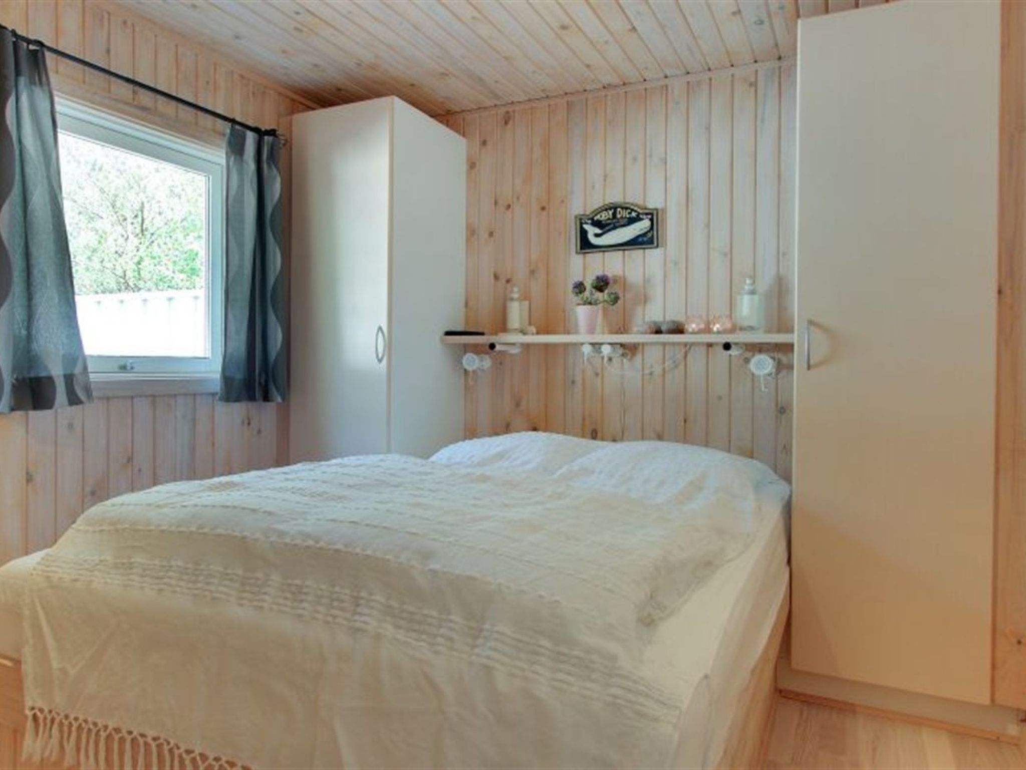 A bedroom with a bed, a wardrobe, a shelf with toiletries, and a window with curtains.