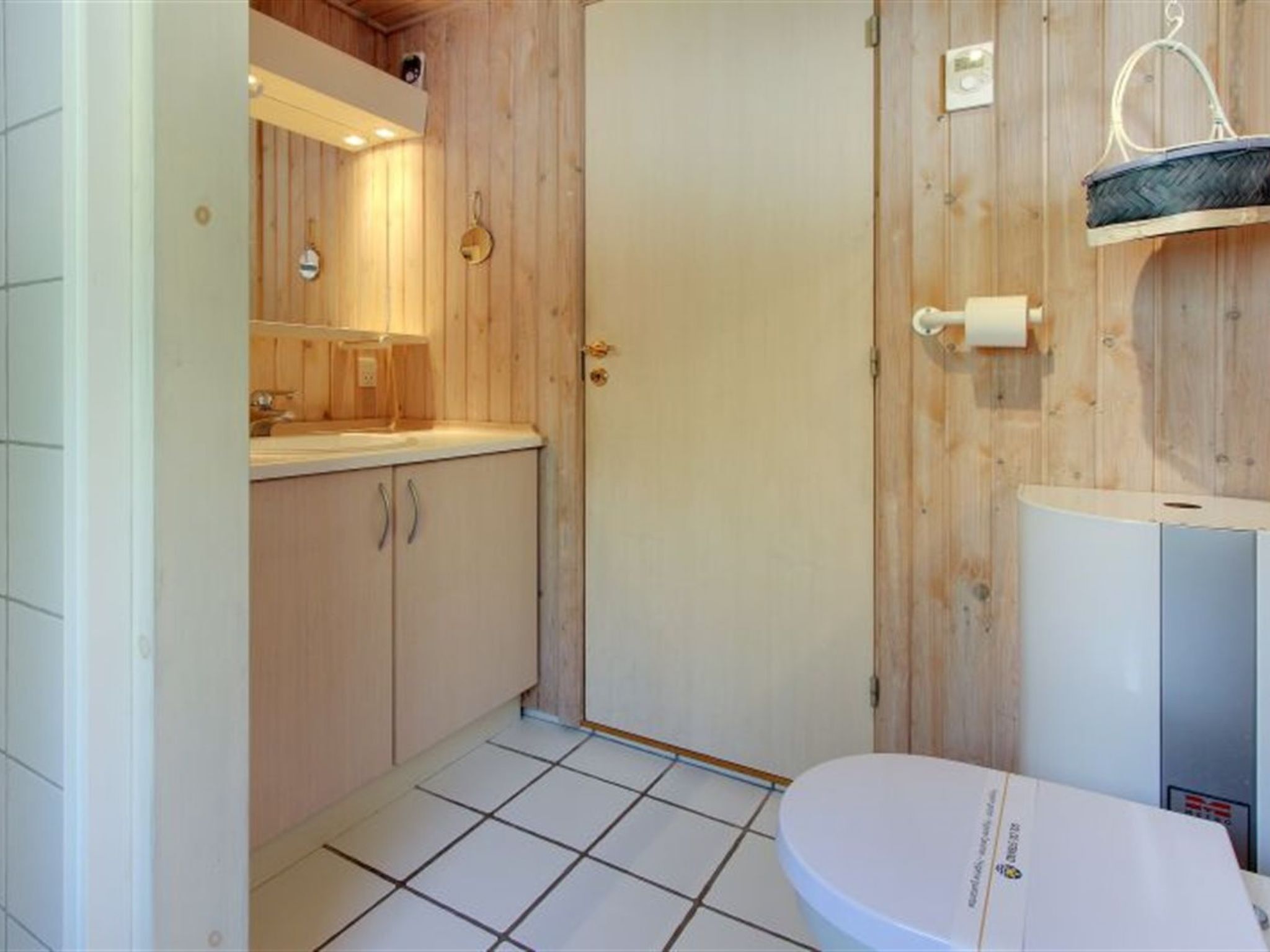 Un baño con paneles de madera, un inodoro blanco, un lavabo con espejo y un perchero para toallas.