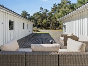 A covered outdoor seating area with wicker furniture and a gravel path leading to a building with a white exterior.