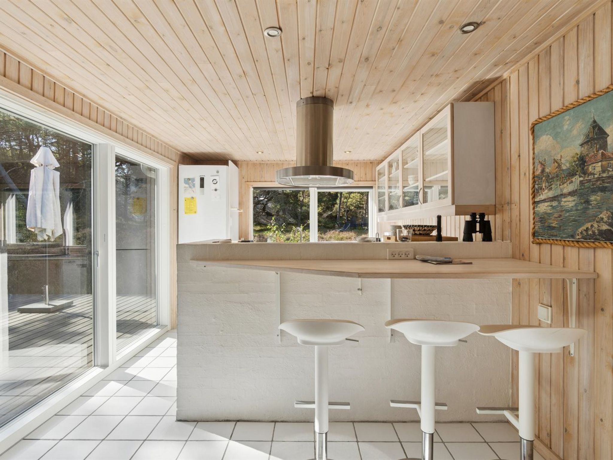 A modern kitchen with a wooden ceiling, a central island with bar stools, and a view of the outdoors.