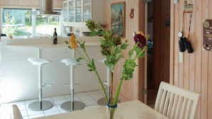 A dining area with a white table, two bar stools, a vase with flowers, and a window with a view of greenery. - "Minka" - 300m from the sea by Interhome (Nexø)