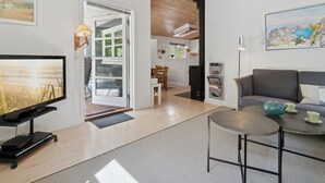 Una sala de estar moderna con un televisor de pantalla plana, un sofá, una mesita redonda y una cocina con estufa.