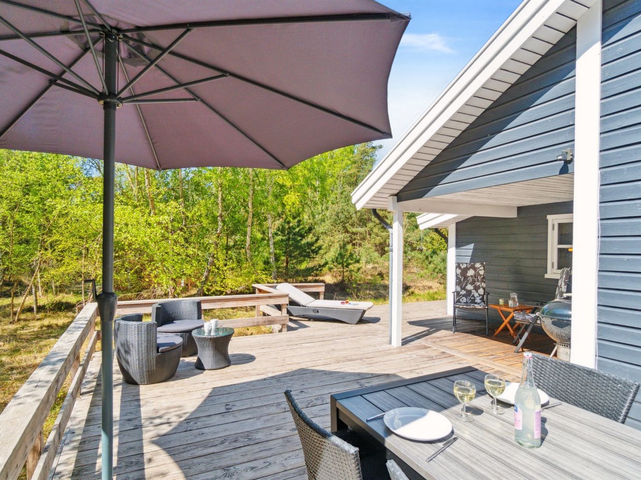 A covered outdoor patio with a table set for dining, surrounded by chairs and a large umbrella.