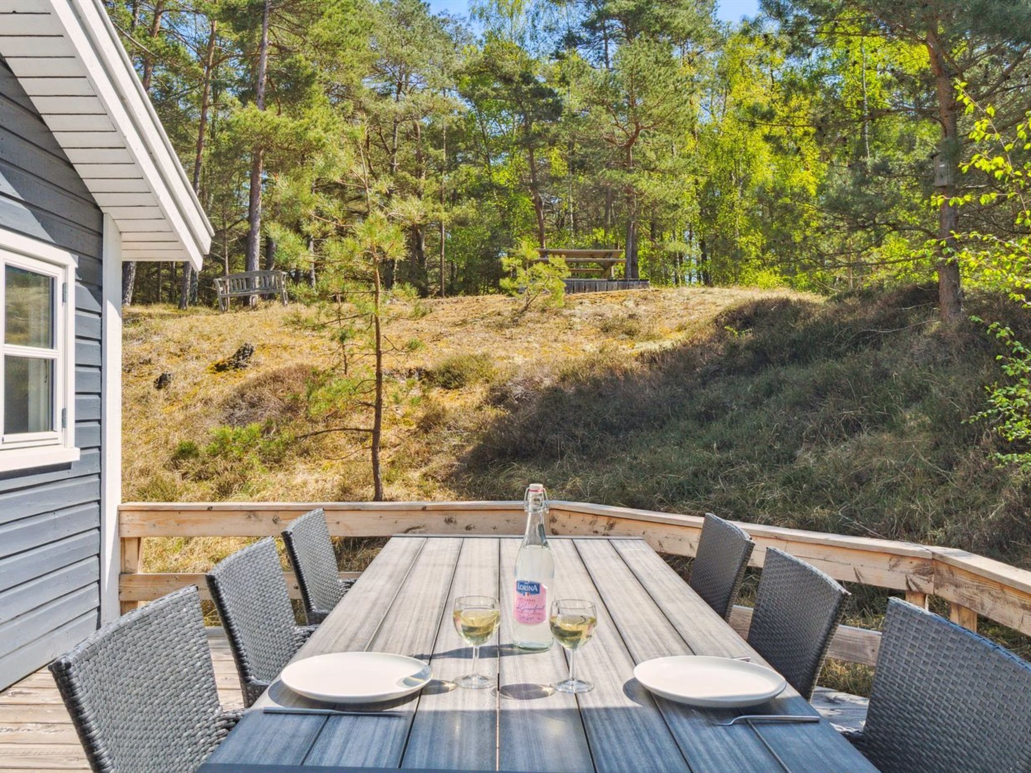 Eine Holzterrasse mit einem Tisch für zwei Personen mit Blick auf einen bewaldeten Hügel.