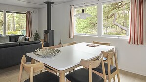 A modern dining area with a white table and wooden chairs, a black stove, and large windows with curtains. - "Michel" - 300m from the sea by Interhome (Nexø)