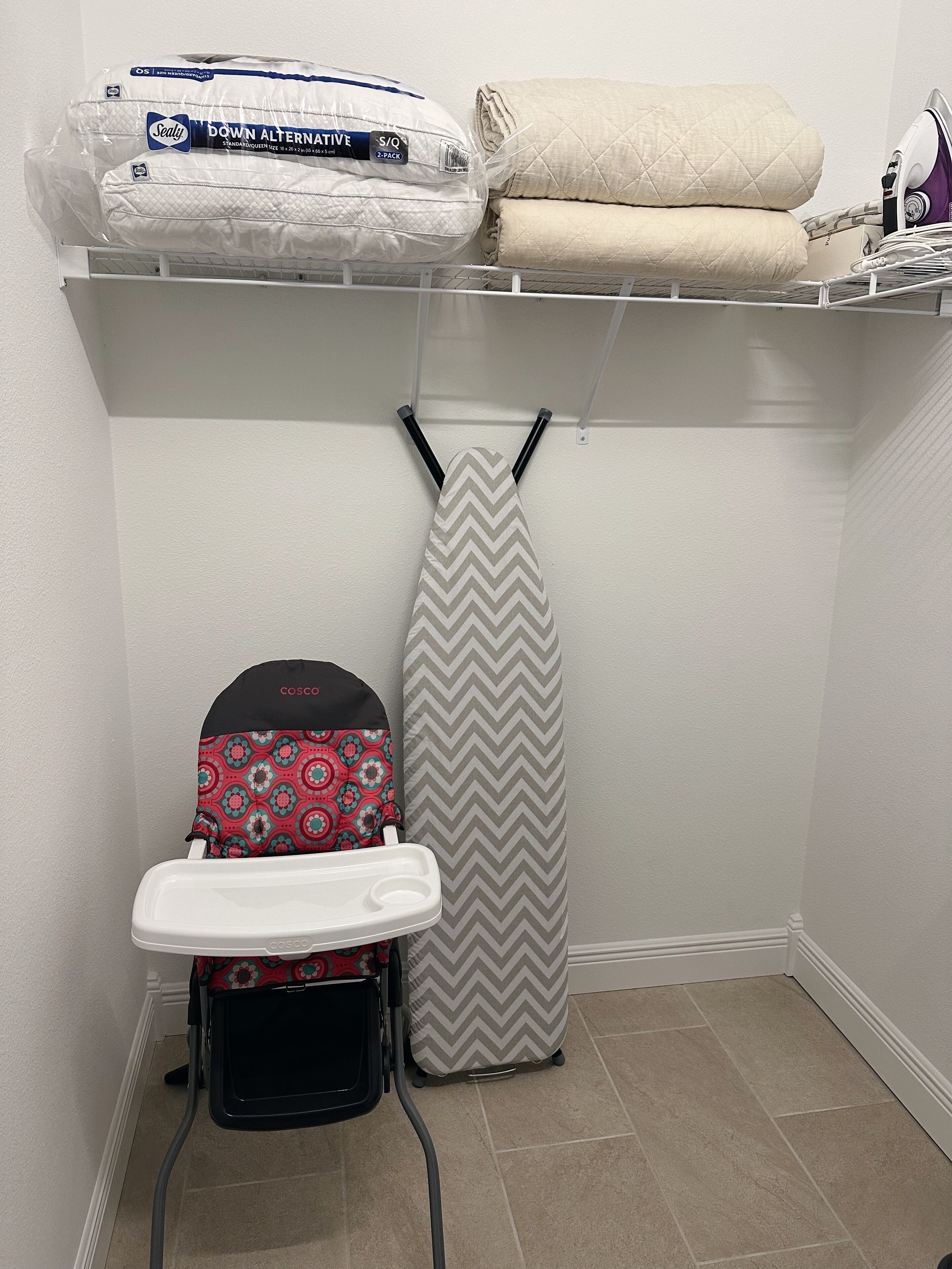 A laundry area with a hanging iron, a baby stroller, and storage shelves with folded blankets.