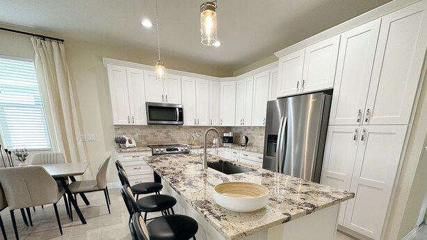 A modern kitchen with white cabinets, a stainless steel refrigerator, a built-in oven, and a granite countertop. - NEW Cozy Home in Historic Venice (Venice)