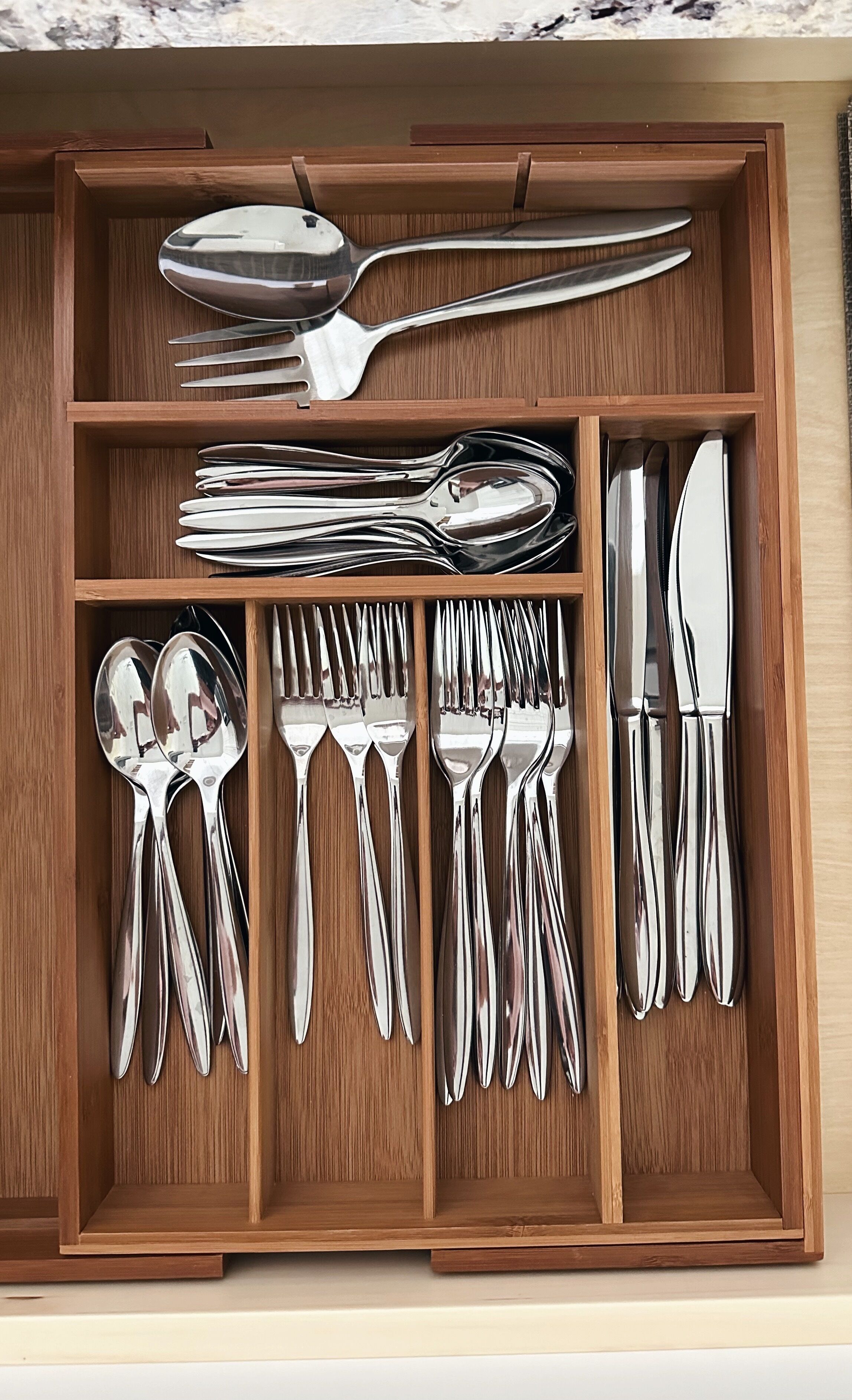 A wooden drawer with neatly arranged silverware including spoons, forks, and knives.