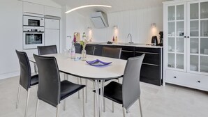 A modern kitchen with white cabinetry, a dining area with a white table and black chairs, and a white cabinet with glass doors. - "Botolphus" - 20m from the sea by Interhome (Nexø)
