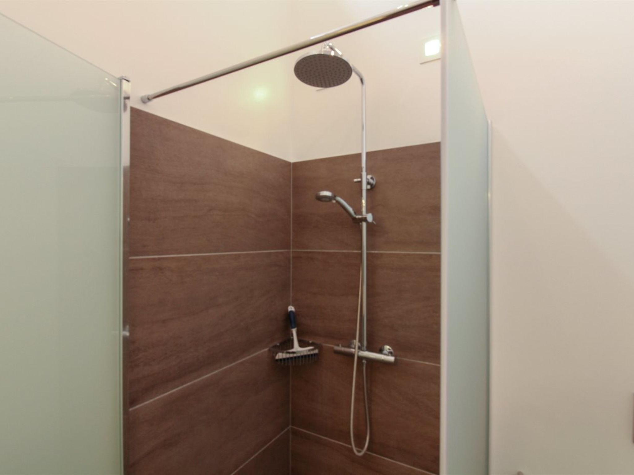 A shower with a handheld showerhead and a wall-mounted faucet.