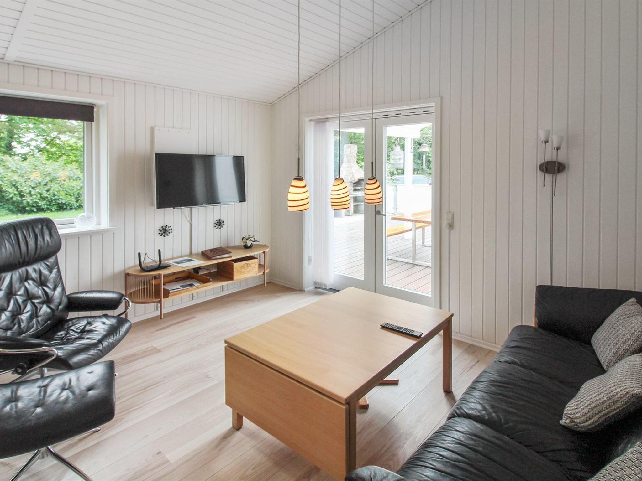 A modern living room with a wooden coffee table, black leather sofa, and a TV mounted on the wall.