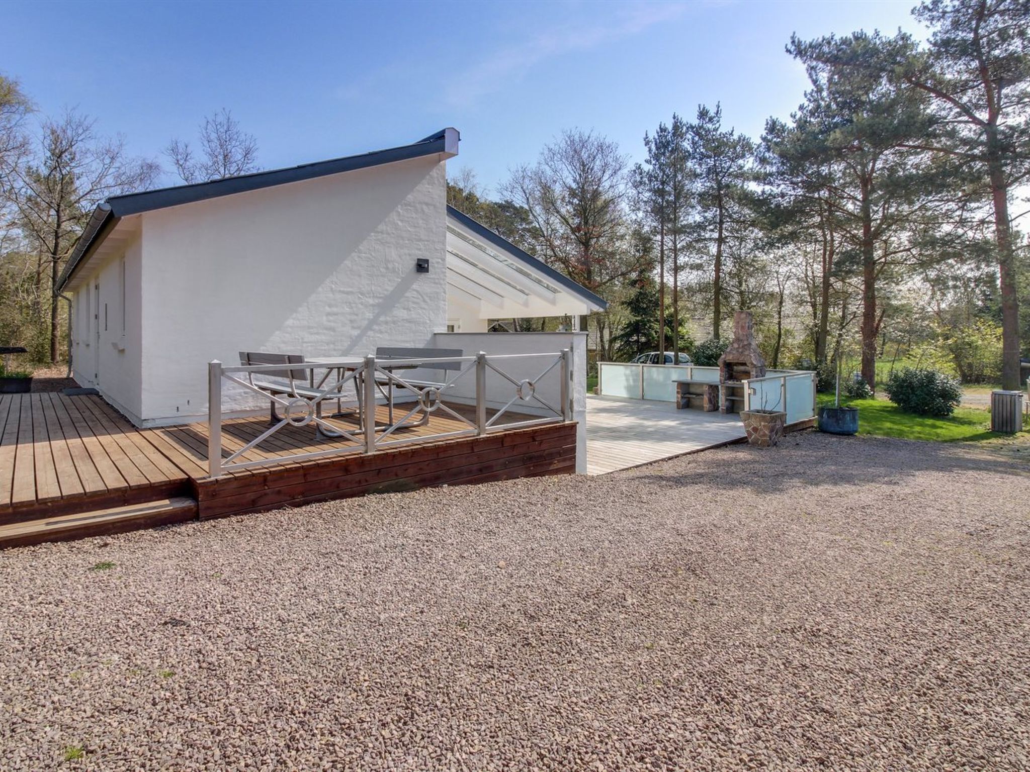Et moderne udendørsområde med træterrasse, grill og pejs af sten.