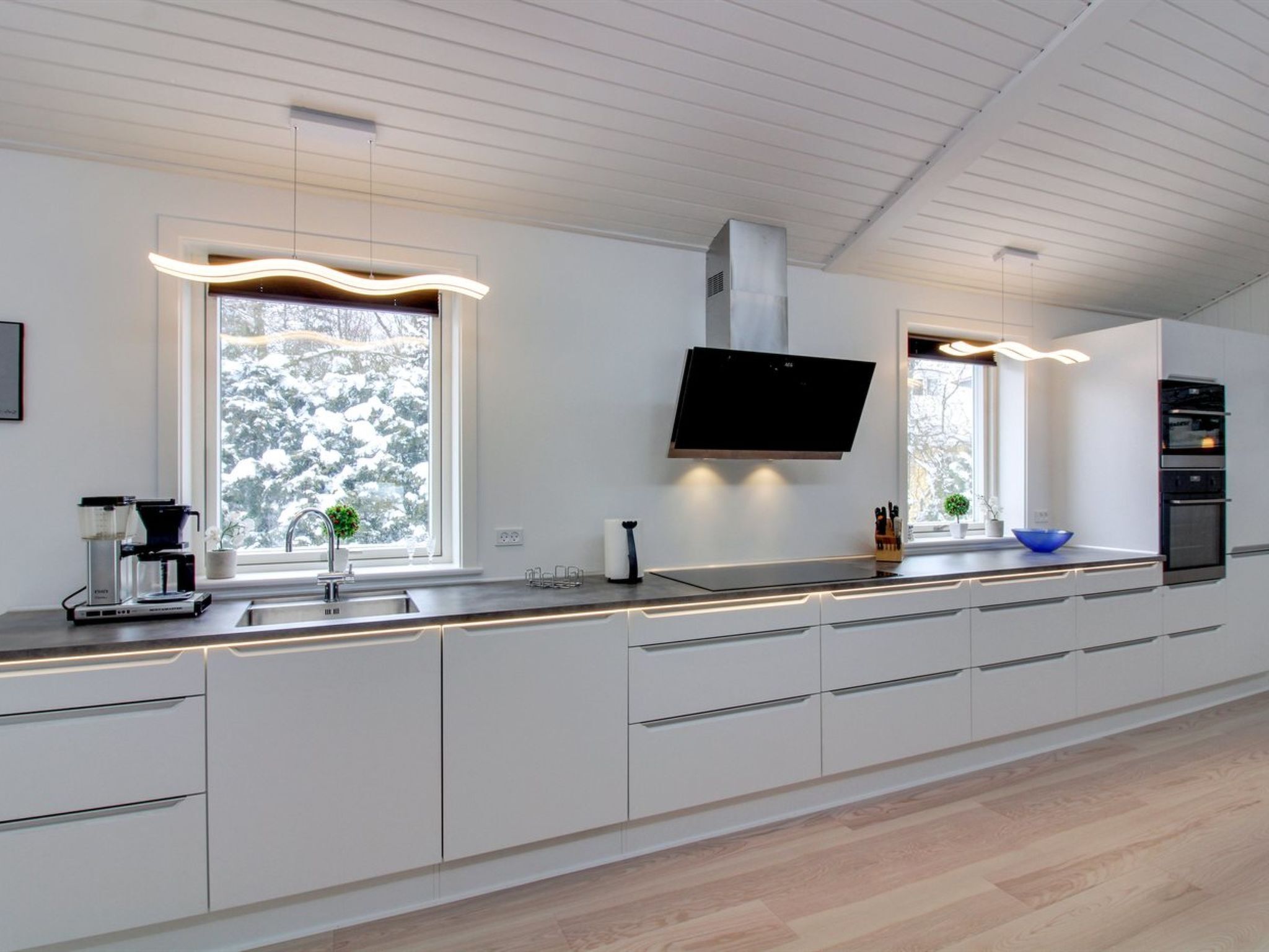 A modern kitchen with white cabinets, a built-in oven, and a flat-screen TV.