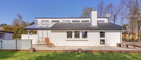 A modern two-story house with a flat roof, large windows, and a covered patio area.