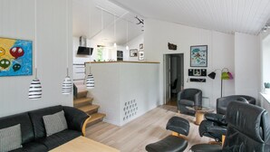 A modern living room with a black leather sofa, a wooden coffee table, and black leather armchairs. A staircase leads to a kitchen area with a TV and a dining table. - "Antigona" - 250m from the sea by Interhome (Nexø)