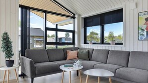 Ein modernes Wohnzimmer mit einem grauen Ecksofa, zwei kleinen weißen Beistelltischen und einer Zimmerpflanze.