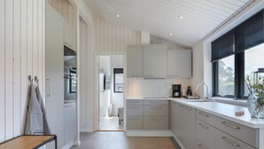 Eine moderne Küche mit hellen Holzschränken, einem großen Fenster und Blick ins Freie.