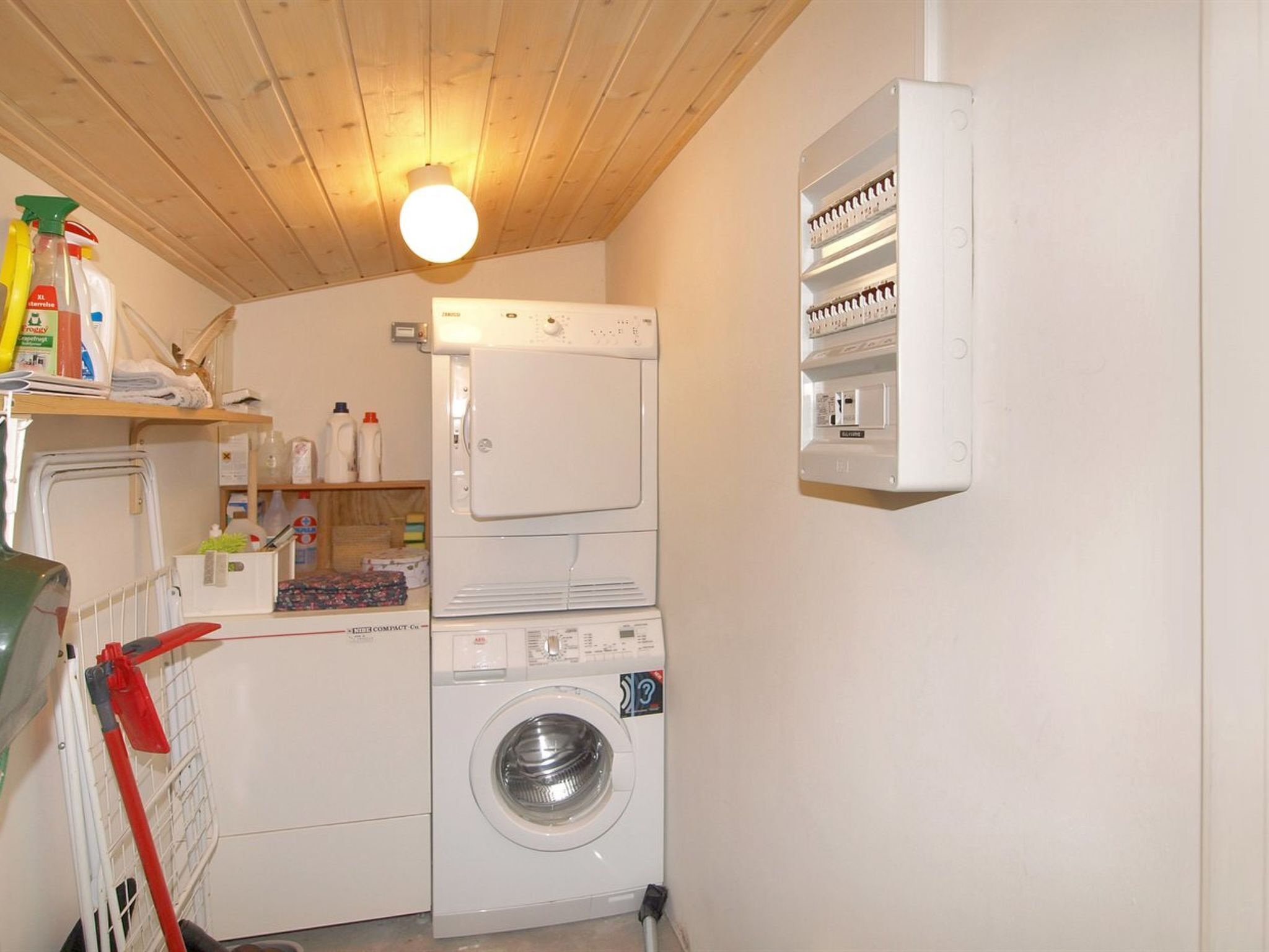 Uma lavanderia compacta com máquina de lavar, secadora e estantes empilhadas com produtos de limpeza.