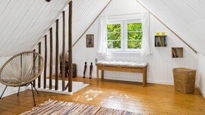 A spacious attic room with a sloped ceiling, wooden beams, a large window with a view of greenery, a woven chair, a bench, and a small bookshelf. - "Hansen" - 5.2km from the sea by Interhome (Aakirkeby)