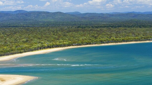 A coastal landscape with clear blue waters, sandy beaches, and a forested background.