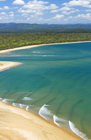 A coastal landscape with clear blue waters, sandy beaches, and a forested background.