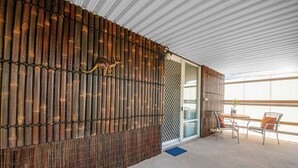 A modern interior with a bamboo wall, a glass door leading to a balcony, and a seating area with two chairs and a table.