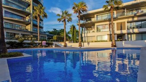 Un hotel modern amb una piscina envoltada per palmeres i un cel blau clar.