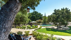 Um pátio com cadeiras de descanso, piscina e um gazebo, tudo cercado por árvores e vegetação.