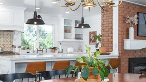 Uma cozinha moderna com armários brancos, parede de destaque em tijolo e uma área de refeições com mesa e cadeiras de madeira.