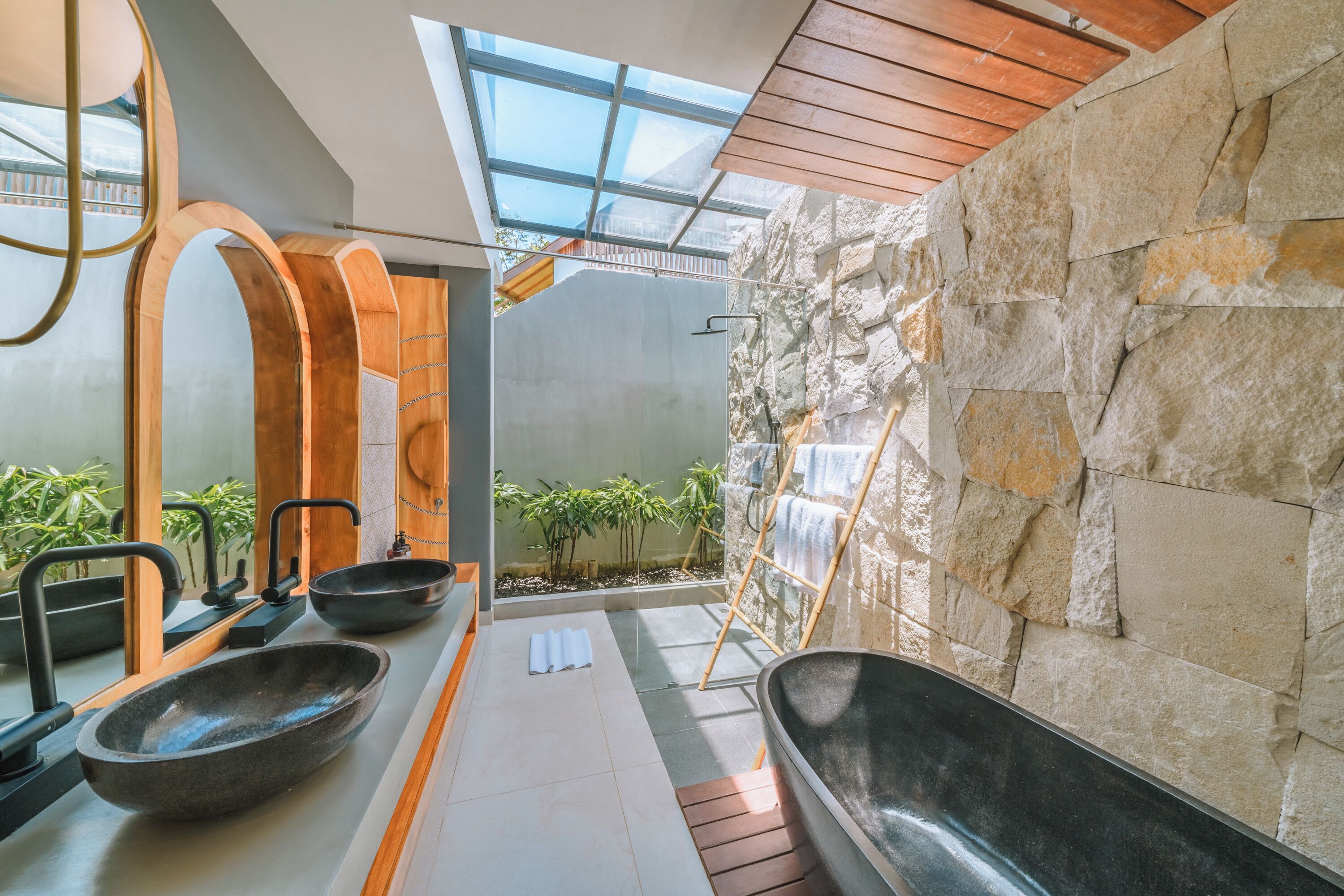 A modern bathroom with a stone wall, a skylight, and two large tubs.