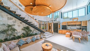 A spacious living area with a staircase, a large wooden ceiling, and a kitchen area with wooden furniture. - Villa Asri -  Tropical 3BR Villa (Tabanan)