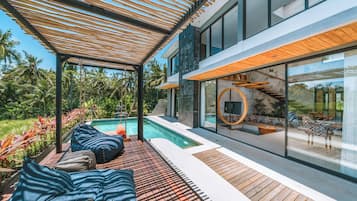 A modern outdoor pool area with wooden decking, lounge chairs, and a glass-enclosed staircase.