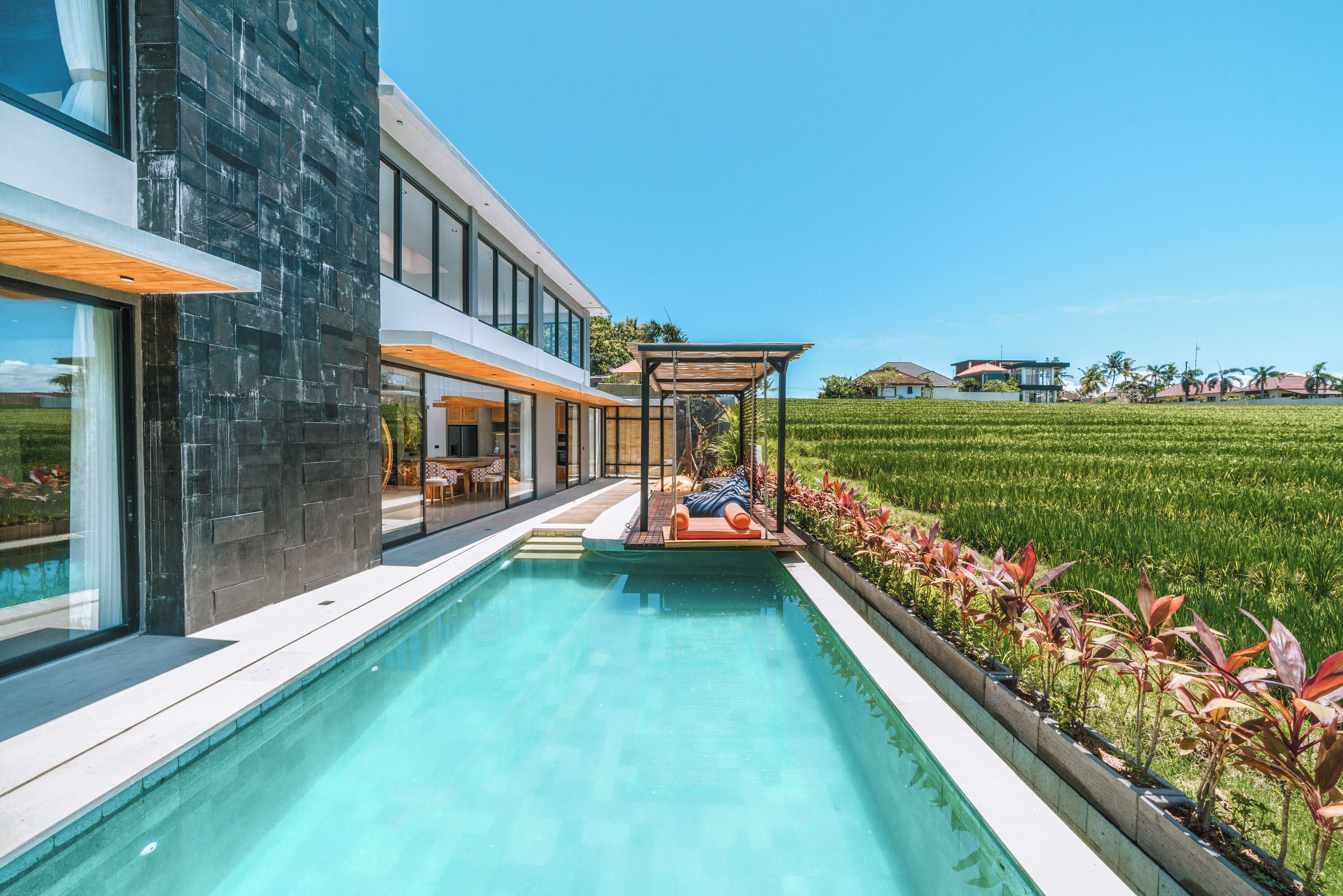 A modern house with a swimming pool, a covered outdoor seating area, and a view of a green field.