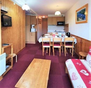 Ett kompakt bostadsutrymme med en matplats, ett kök och en liten sittgrupp.