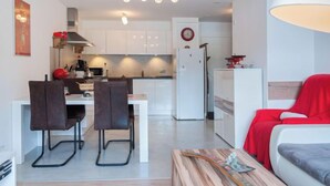 Eine moderne Küche mit weißen Schränken, ein Essbereich mit zwei Stühlen und ein rotes Sofa im Wohnzimmer.